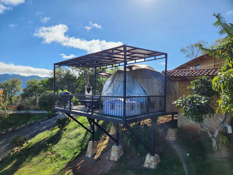 El domo geodésico sobre una plataforma elevada con techo propio, jacuzzi en la terraza y las montañas del valle de fondo