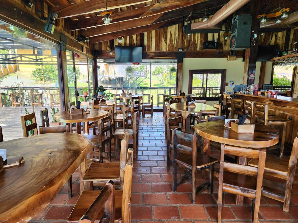 Comedor interior con mesas y sillas de madera rústica, piso de ladrillo y la barra al fondo