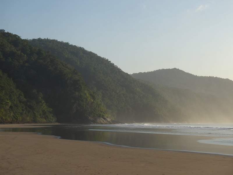 Cordilleras boscosas que bajan hasta el mar en capas de neblina, con la playa ancha descubierta por la marea baja